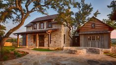 a stone house with two trees in front of it and a walkway leading to the entrance