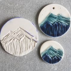 three ceramic ornaments with mountains on them sitting on a gray surface next to each other