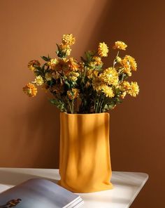 a yellow vase filled with flowers sitting on top of a table next to a book