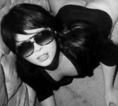 a woman laying on top of a bed wearing sunglasses