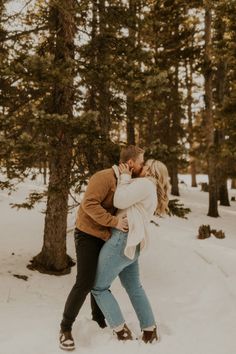 a couple kissing in the snow surrounded by trees