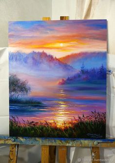 an easel with a painting on it that has a sunset in the background and water