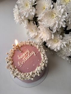 a pink birthday cake sitting next to white flowers