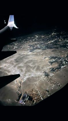 the wing of an airplane flying over a city at night with clouds and lights on it