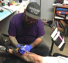 a man getting his tattoo done by another person in a room with other items on the table