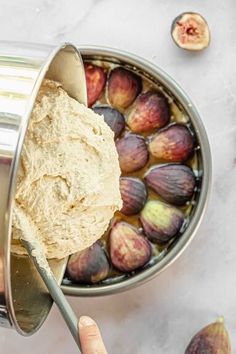 a hand holding a spoon over a bowl of hummus next to some figs