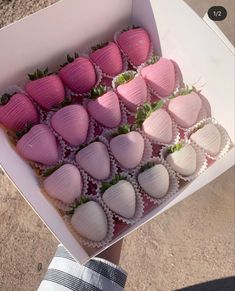 a box filled with pink and white chocolate covered strawberries next to a person's hand