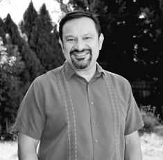 a black and white photo of a man smiling at the camera with trees in the background