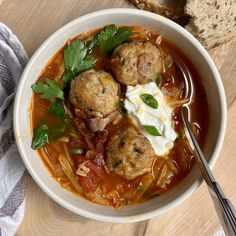 a bowl of soup with meatballs, sour cream and parsley in it on a wooden table