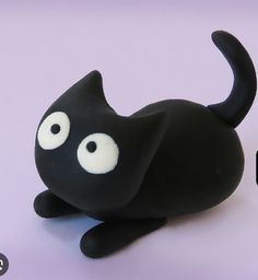 a black cat figurine sitting on top of a white table next to a cell phone