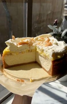 a person holding a cake in front of a window with one slice missing from it