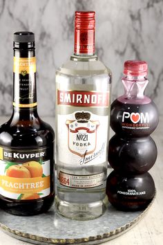 three bottles of alcohol sitting on top of a marble tray next to two black balls