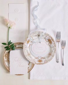 a table setting with white and gold plates, silverware, napkins and flowers