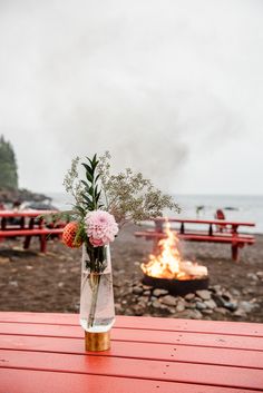 a vase filled with flowers sitting on top of a red table next to a fire pit