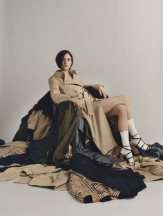 a woman sitting on top of a pile of clothes wearing high heeled shoes and trench coat