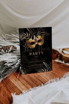 a black and gold masquerade party card sitting on top of a wooden table