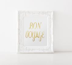 a white frame with the words bon voyage written in gold on it, sitting on a shelf