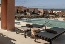 two lounge chairs sitting next to a swimming pool on top of a cement patio near the ocean