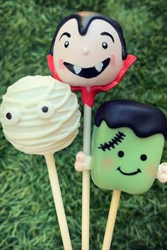 three cake pops with faces on them sitting in the middle of some green grass next to each other