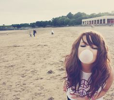 a girl blowing bubbles on the beach with people in the background and buildings behind her