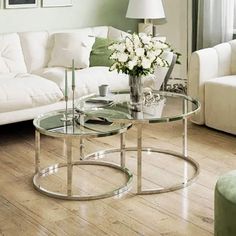 a glass table with flowers on it in front of a white couch and coffee table