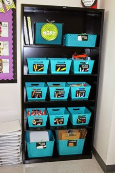 a bookcase filled with lots of blue bins next to a pile of books