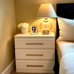 a bedroom with a bed, nightstand and lamp on top of the night stand in front of it