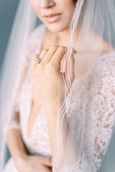 a woman wearing a wedding veil with a diamond ring on her finger and holding onto the side of her veil