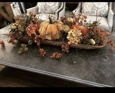 an arrangement of pumpkins and gourds on a table with chairs in the background