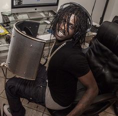 a man with dreadlocks sitting in front of a computer desk holding a speaker