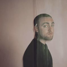 a man with green hair is standing in front of a pink wall