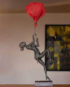 a metal statue with a red balloon attached to it's head and feet on a wooden table