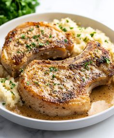 two pork chops with mashed potatoes and parsley in a white bowl on a marble surface