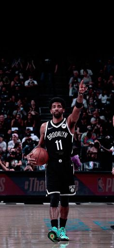 a basketball player holding a ball in his right hand while walking across a court with people watching