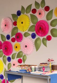 a table topped with lots of paper flowers next to a wall covered in green leaves