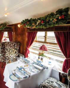 a dining car with christmas decorations on the ceiling and table set for two, along with matching chairs