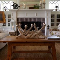 a wooden table with candles on it in front of a fire place and couches