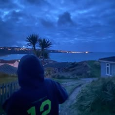 a person wearing a hoodie looking out at the ocean and houses in the distance