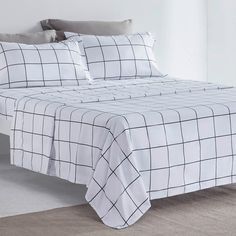 a bed with white sheets and black checkered pattern on the comforter, along with two pillows