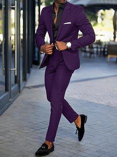 a man in a purple suit and black shoes is walking down the street with his hand on his hip