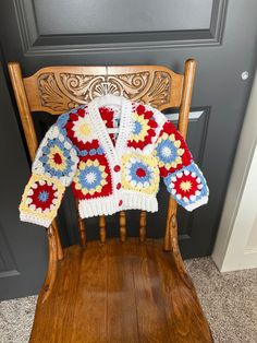 a crocheted sweater sitting on top of a wooden chair next to a door