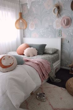 a white bed with pink and grey pillows in a bedroom next to a wallpapered wall