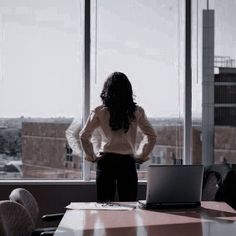 a woman standing in front of a window with her hands on her hips looking out the window