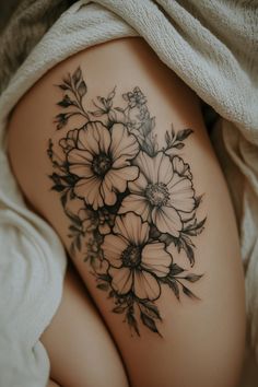 Floral tattoo on a person's thigh, partially covered by a white blanket. Top Leg Tattoo Women, Women’s Leg Tattoo Floral, Floral Tattoo Thigh Hip, Edgy Symbols, Top Of Thigh Tattoo, Thigh Tatoos Woman, Lower Thigh Tattoo, Thigh Tattoo Flowers, Floral Thigh Tattoos Women