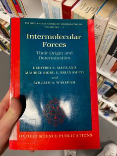 a person holding up a red book in front of bookshelves with information on them