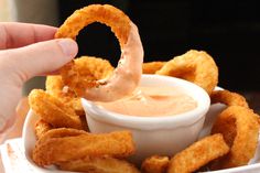 a person dipping something into a bowl with onion rings