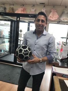 a man is holding a soccer ball in his right hand and smiling at the camera