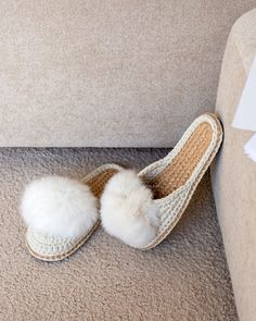 a pair of white slippers sitting on top of a carpeted floor next to a beige couch