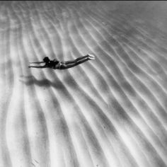 black and white photograph of a woman swimming in the sand