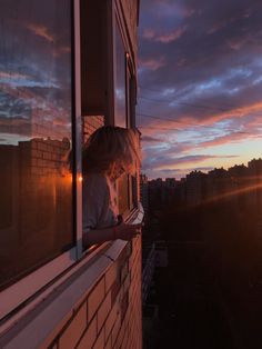 a woman is looking out the window at the sunset